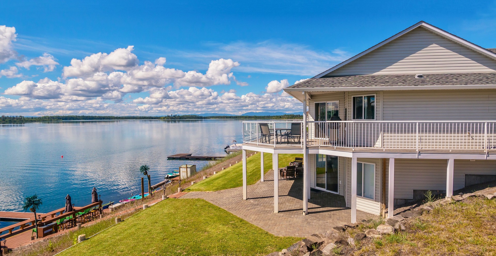 Wide angle view of a beautiful, large modern luxury summer holiday home, featuring sun decks, glass railings and large windows, set beside a freshwater lake in central British Columbia, Canada.