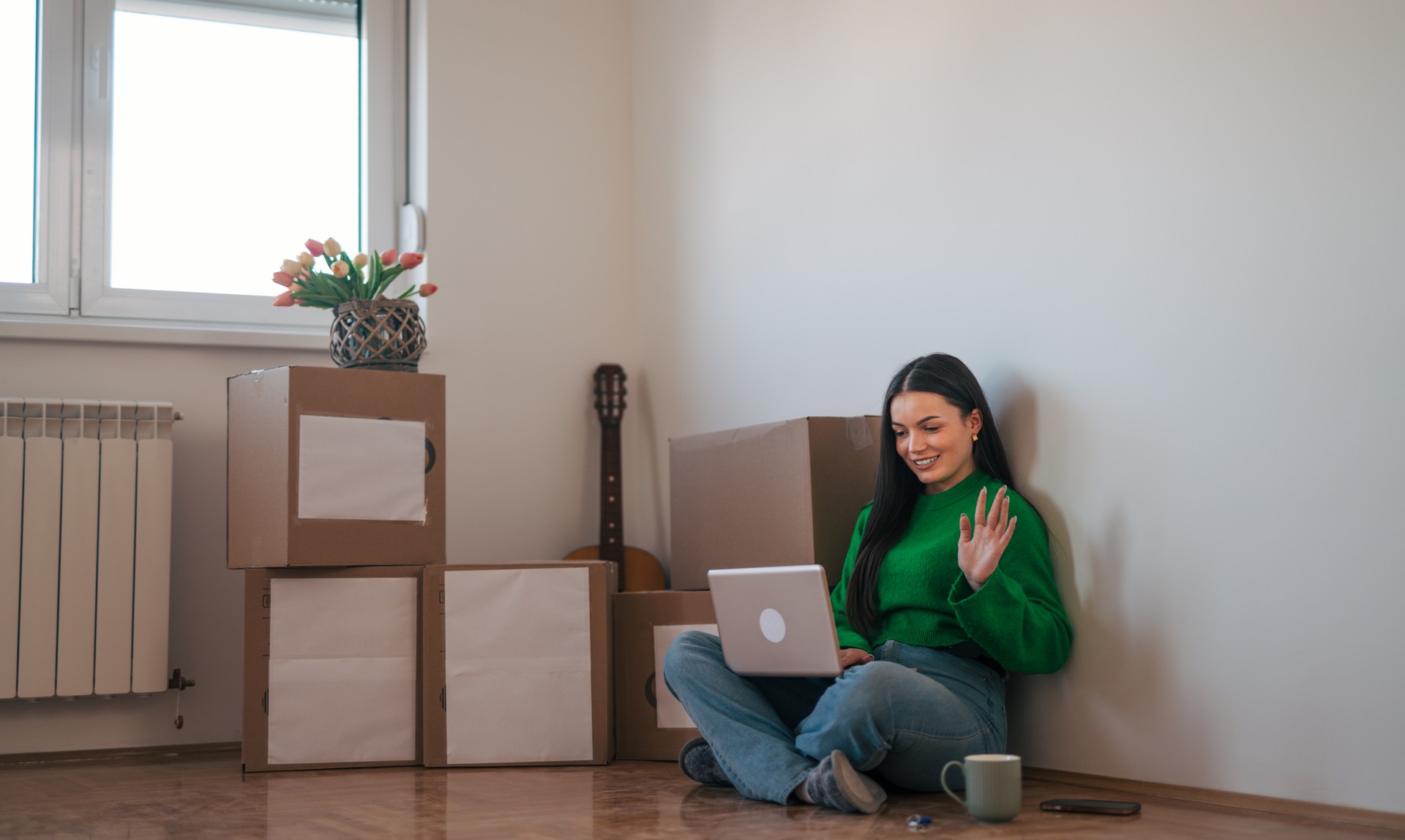 A young beautiful woman is sitting on the floor in her new apartment.