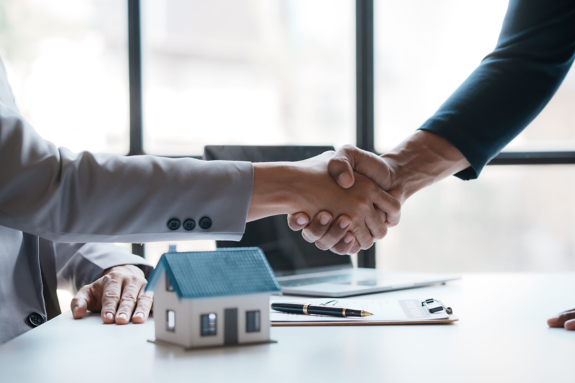 Real estate agent shakes hands with a client to sign a home purchase contract congratulating the client on the purchase.